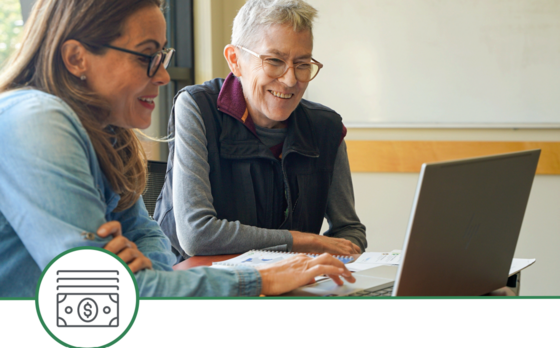 Two people smile as they sit and look at a computer