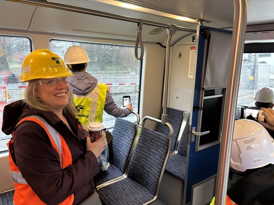 Councilmember Balducci on a light rail train in a hardhat holding a cup of coffee