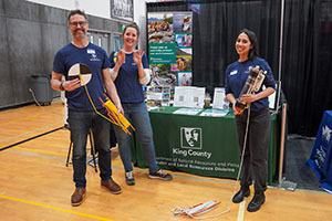 Three people standing in front of a table with a King County logo holding environmental sampling equipment