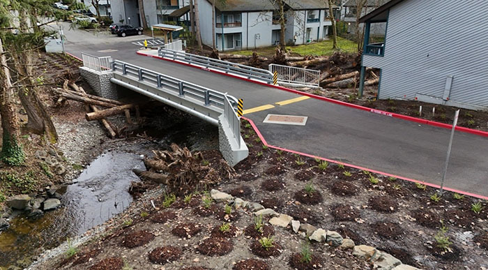 A small stream with a new-looking bridge and plantings near a few houses