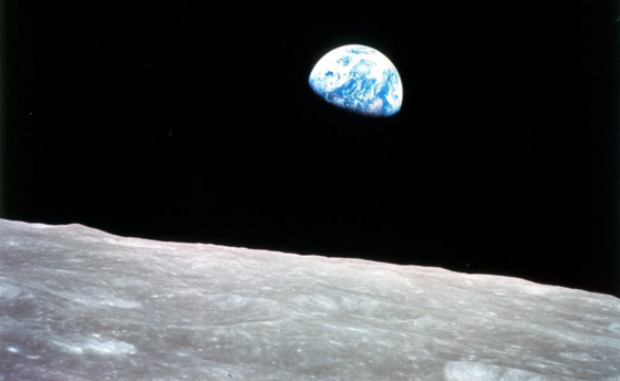 View of Earth from the Moon called Earthrise, showing the planet as a crescent in the blackness of space above a gray, rocky lunar surface.
