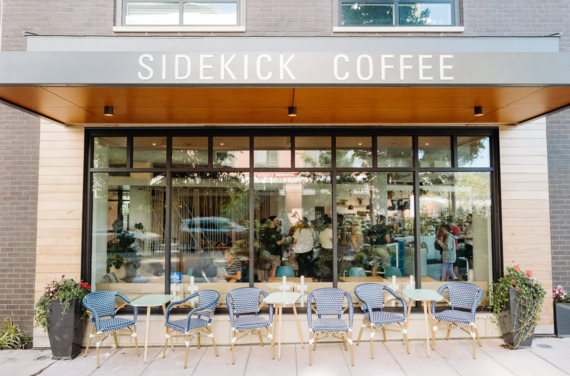 Storefront with floor to ceiling windows and a grey sign with white text above reading Sidekick Coffee.