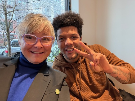 Close up photo of two people smiling and one holding up two fingers in a peace sign.