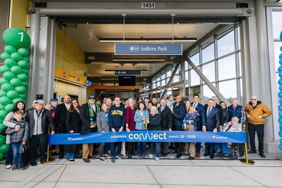 A crowd of people stand at a light rail station in front of a blue ribbon