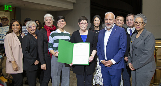 A group of people stand in King County Council Chambers displaying proclamations in green folders