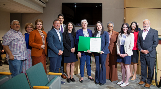 Councilmembers join community members in a group photo inside council chambers holding up a printed recognition for the Iranian community.