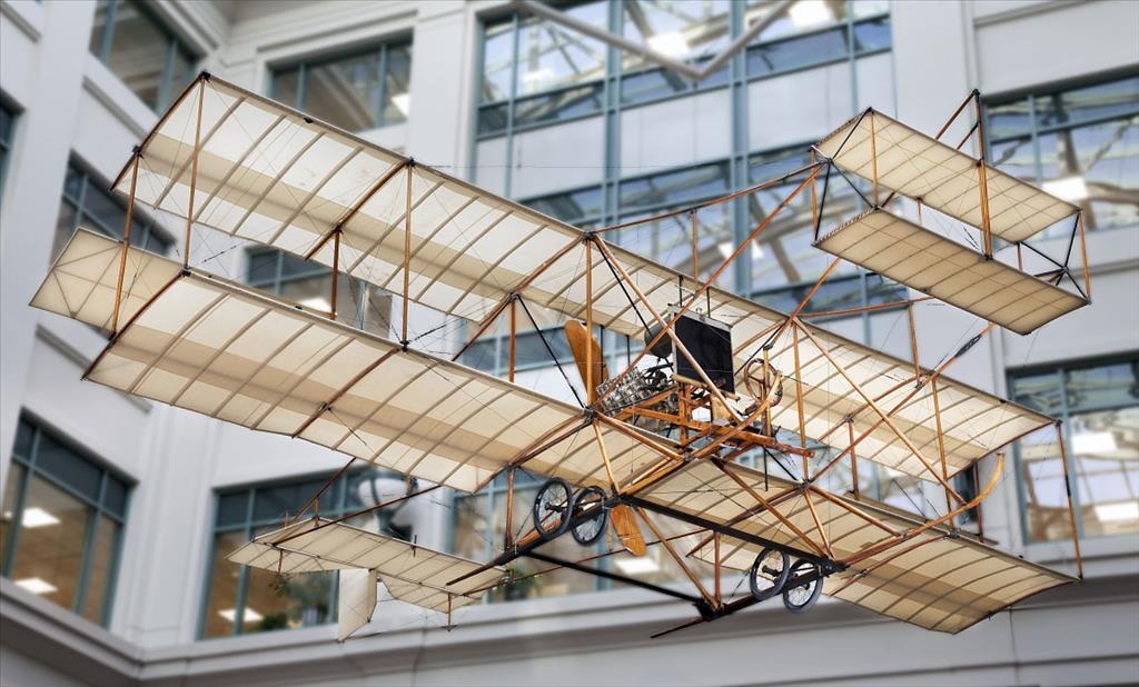 A photo of the Wiseman-Cooke aircraft hangs suspended indoors, showcasing its wooden frame and fabric wings.