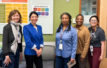 Steffanie standing alongside 4 other women in a bright green conference room