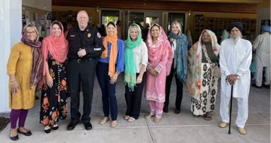 Steffanie standing alongside eight other individuals wearing a bright orange scarf and blue shirt
