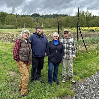 Four people stand in the grass in front of a field with trees in the distance.