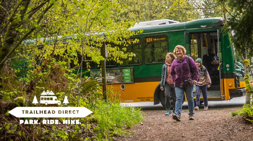 image of the Trailhead direct bus at stop letting three women depart with trailhead direct logo "Park. Ride. Hike."