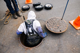 worker in personal protective equipment is lowered into a sewer to inspect pipes
