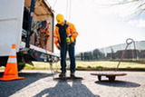 conveyance inspection team looks into a sewer pipe, with a traffic cone in the foreground