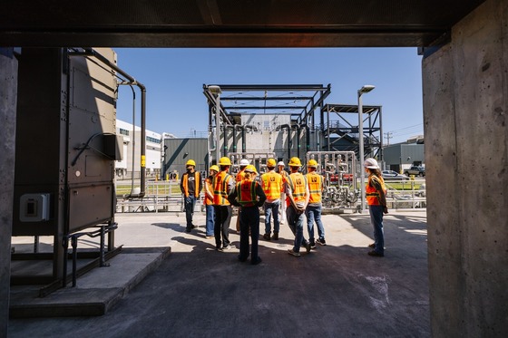 people wearing orange vests and yellow hard hats are guided through a tour of a treatment plant