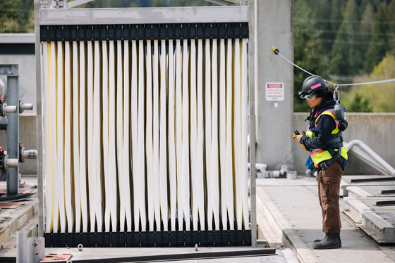 An operator in personal protective equipment operates a crane to move a piece of equipment.