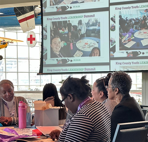 A photo showing Councilmember Lewis sitting with and listening to students at the Youth Leadership Summit.