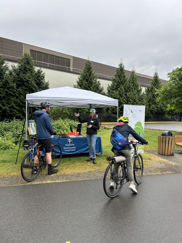 A photo of a King County WTD member talking with two people on bicycles at the King County WTD table at Bike Everywhere Day, 2026.