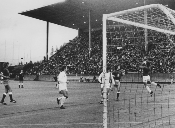 A black and white photo of Sounders debut soccer game in a stadium with spectators in the stands and players on the field near the goal in 1974.