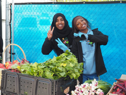 Mawahib Ismail and Derartu Massey holding up a peace sign as they help stock produce at the Rainier Beach Action Coalition Food Hub