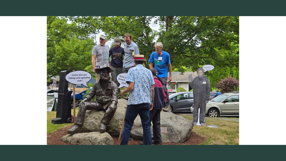 A group of people stand on and around a rock with a dark grey metal statue sitting on it.