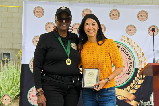 Councilmember Fain posing with an individual holding up an award in front of a sign stating Kent Black Action Commission
