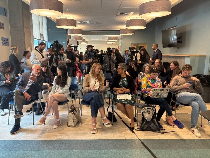 Press Conference room with attendees seated and media teams with cameras 