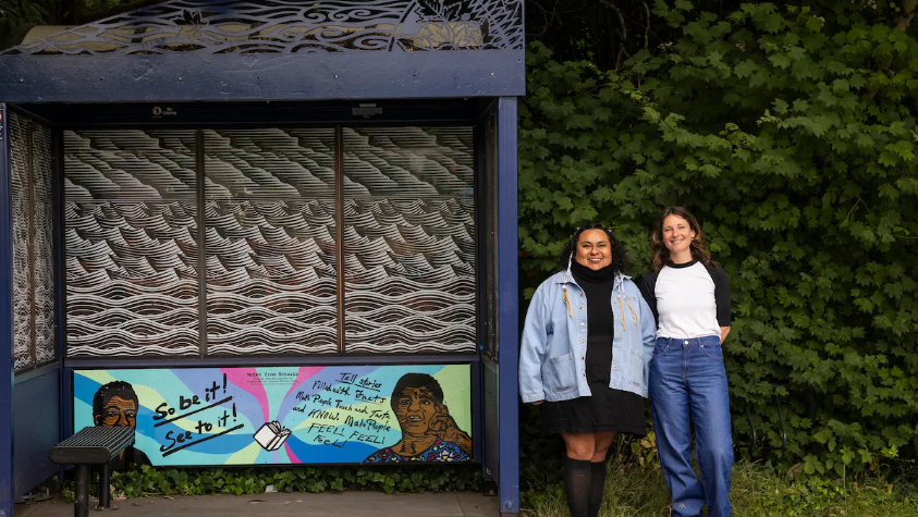 Image of the bus stop with a mural and two people standing beside it