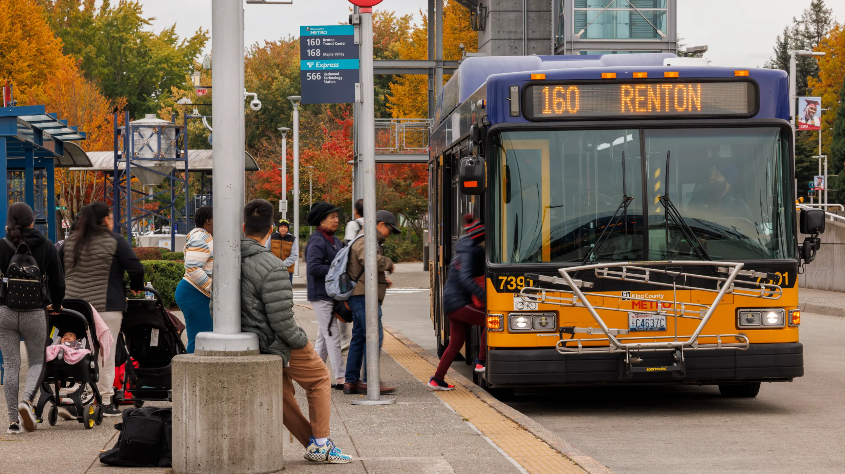 Photo of a busy bus stop at a transit center and a Route 160 bus with destination sign says Renton