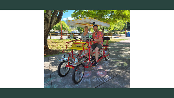 A man and a woman in colorful shirts sitting in a surrey bicycle.