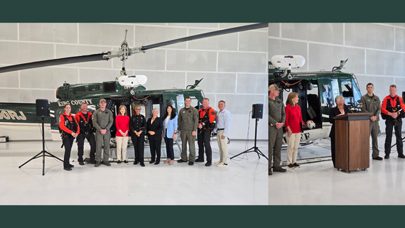 People stand, smiling, in front of a helicopter. Three people are in flight gear.