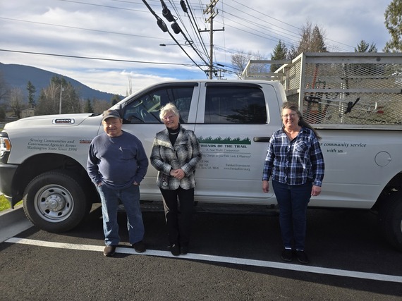 Three people stand in front of a white truck.