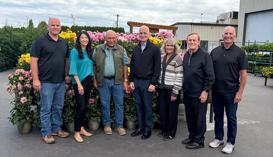 Councilmember Fain standing with seven individuals outside in front of flowers on a cloudy day