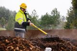 Worker in safety gear rakes steaming compost outdoors.