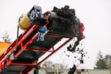 Compost drops from a conveyor in an outdoor processing area.