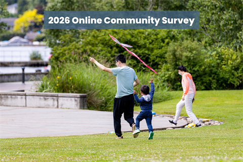An adult and two children frolicking in a park on a field of green grass with a paved area in the background