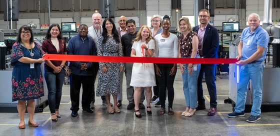 Councilmember Fain standing in front of a ribbon with a dozen other people in a large warehouse
