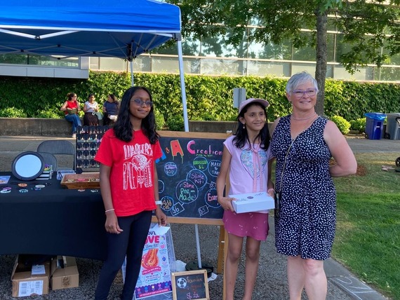 A woman stands with two young girls in front of a blue tent and a sign reading A&A Creations.