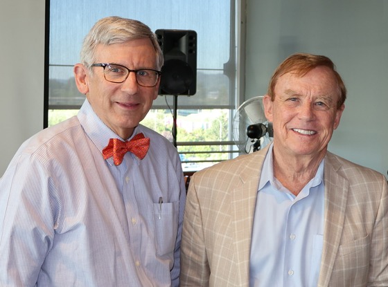 Bob Donegan and Pete von Reichbauer  both wearing light shirts with large windows and a microphone stand behind them.
