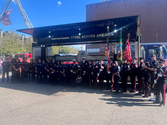 People in first responder uniforms stand in front of flags and a stage saying "Tunnel-Towers Steel Across America"