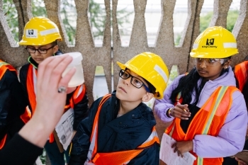 Elementary school students in hardhats are looking at a wastewater sample.