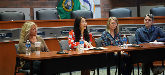 CM. Fain speaking into a microphone with three other individuals sitting at a table in Kent City Hall