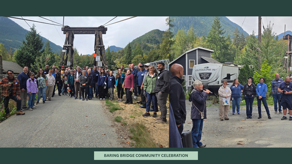 A large group of people gathered at the entrance to a timber suspension bridge.