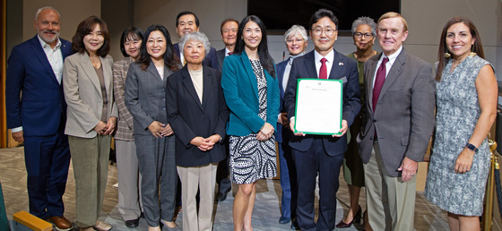 CM. Fain standing with her colleagues and the new Consul General of Korea holding a proclamation