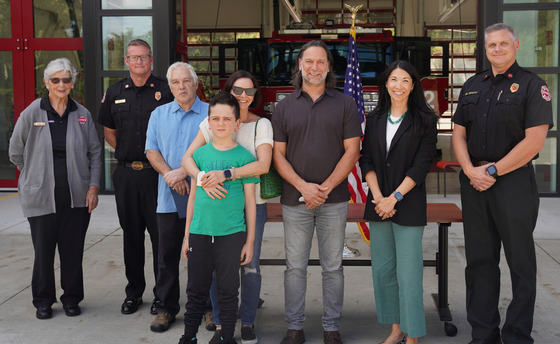 CM. Fain standing in front of a fire station with several other individuals including multiple firefighters