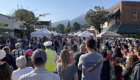 A crowd of people stand, watching a parade walk by on a sunny day.