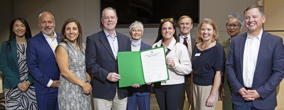A photo with one person holding a green folder and certificate while others stand and smile.
