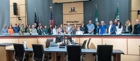 A large group of people standing behind a dais with the King County logo behind them
