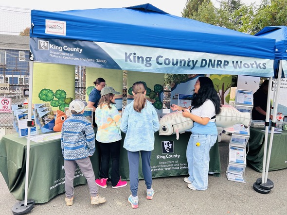 Photo of two King County staff members talking with three children visiting our booth at Salmon Days