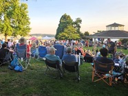 Image shows people sitting in the grass, enjoying an evening summer concert at Marina Park