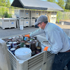 Household hazardous waste facility staff member places paint into bin for recycling.